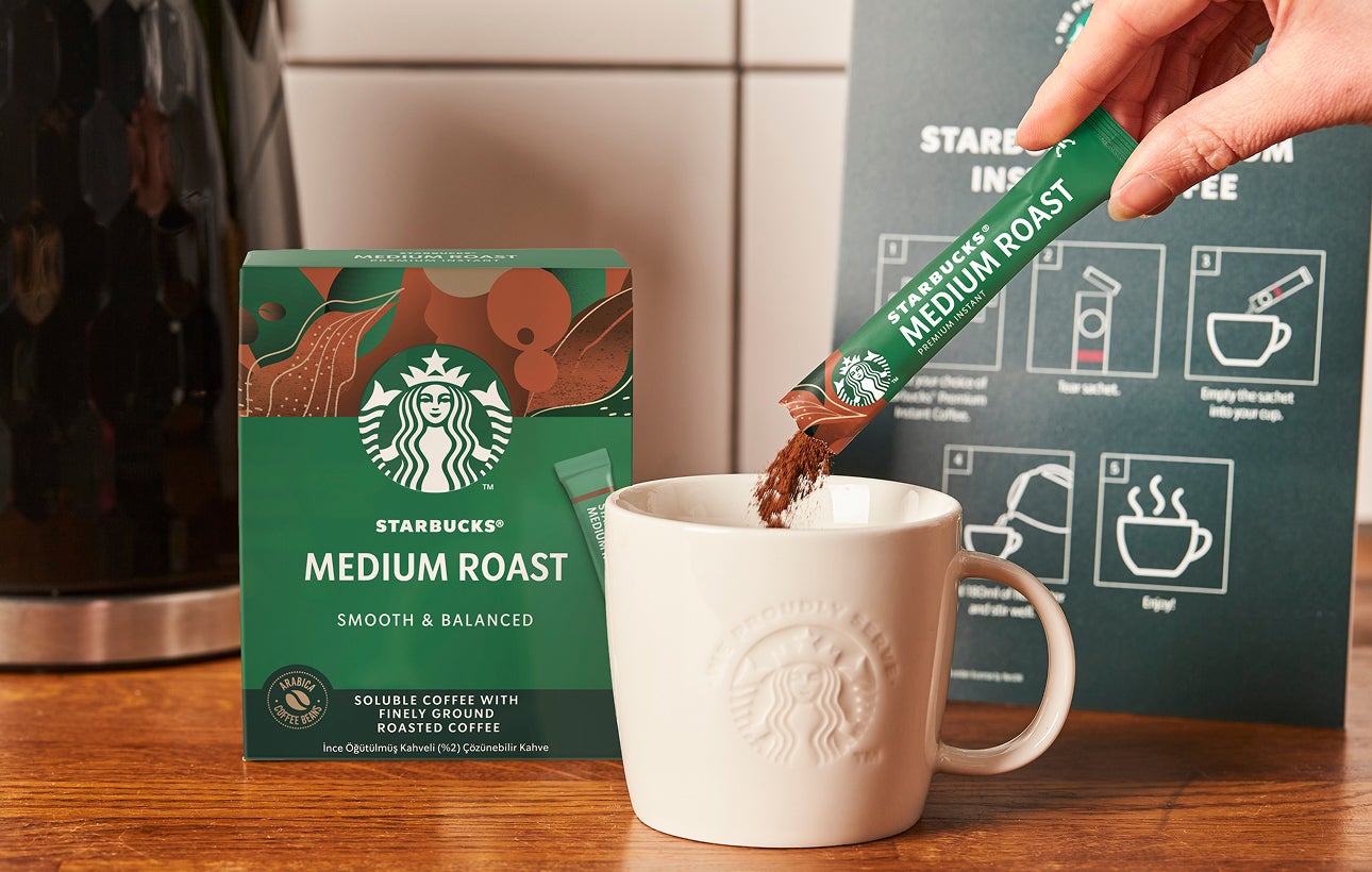 Et Starbucks Premium Instant Medium Roast-kaffebrev hældes i et We Proudly Serve Starbucks-keramikkrus 