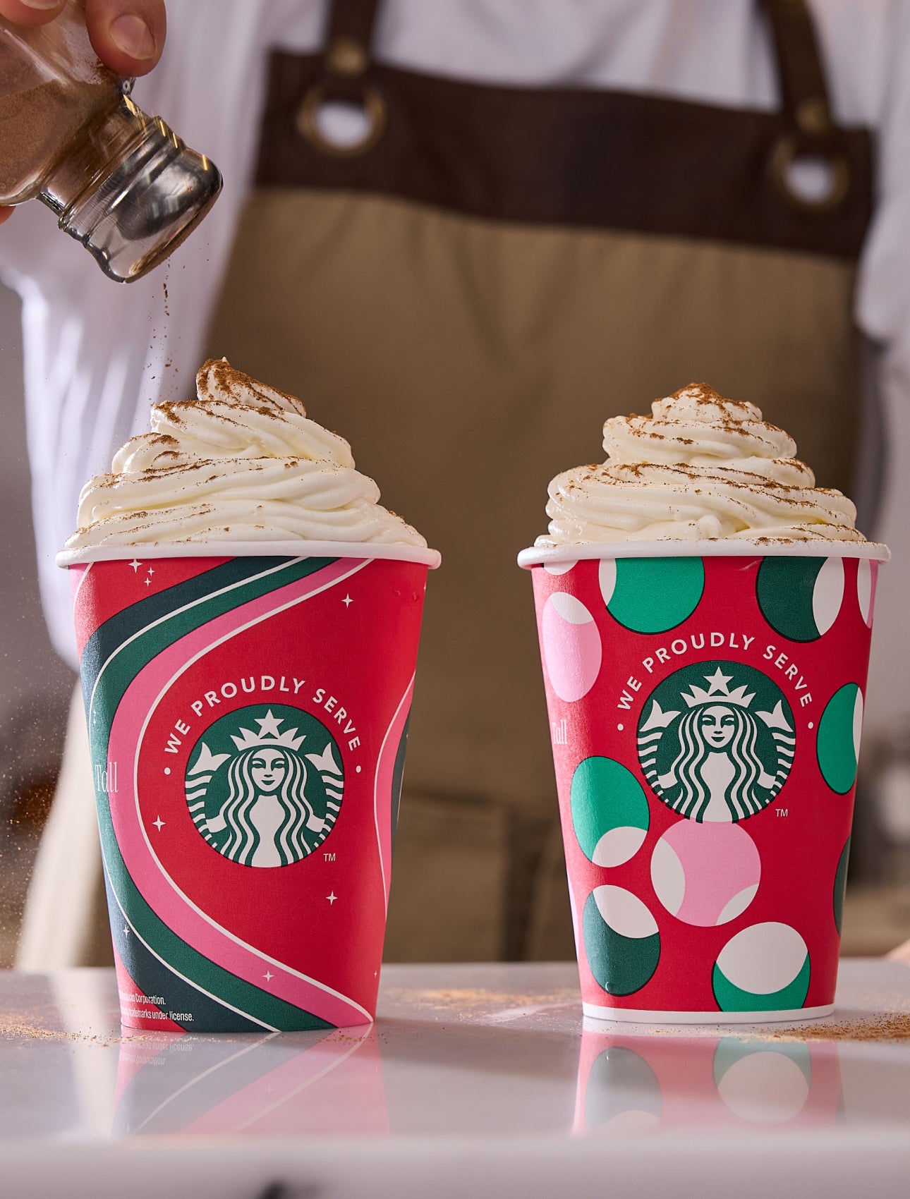 To Frappuccino® Blended Beverages i We Proudly Serve Starbucks-bægre, der passer til højtiden, med kanel drysset over den ene