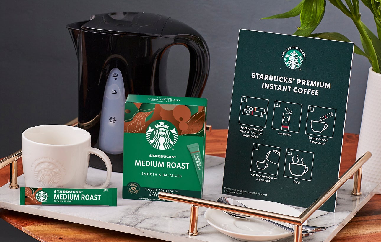 En bordplade med et We Proudly Serve Starbucks-krus, Starbucks Premium Instant Coffee og en tilberedningsvejledning