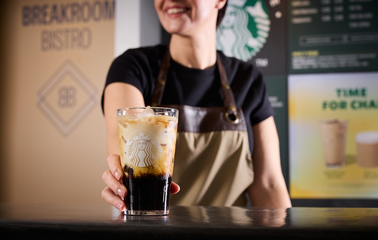 En barista serverer We Proudly Serve Starbucks-iskaffe med et lag af kaffe og fløde
