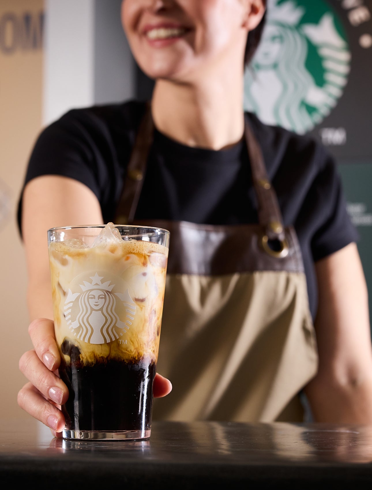 En barista serverer We Proudly Serve Starbucks-iskaffe med et lag af kaffe og fløde