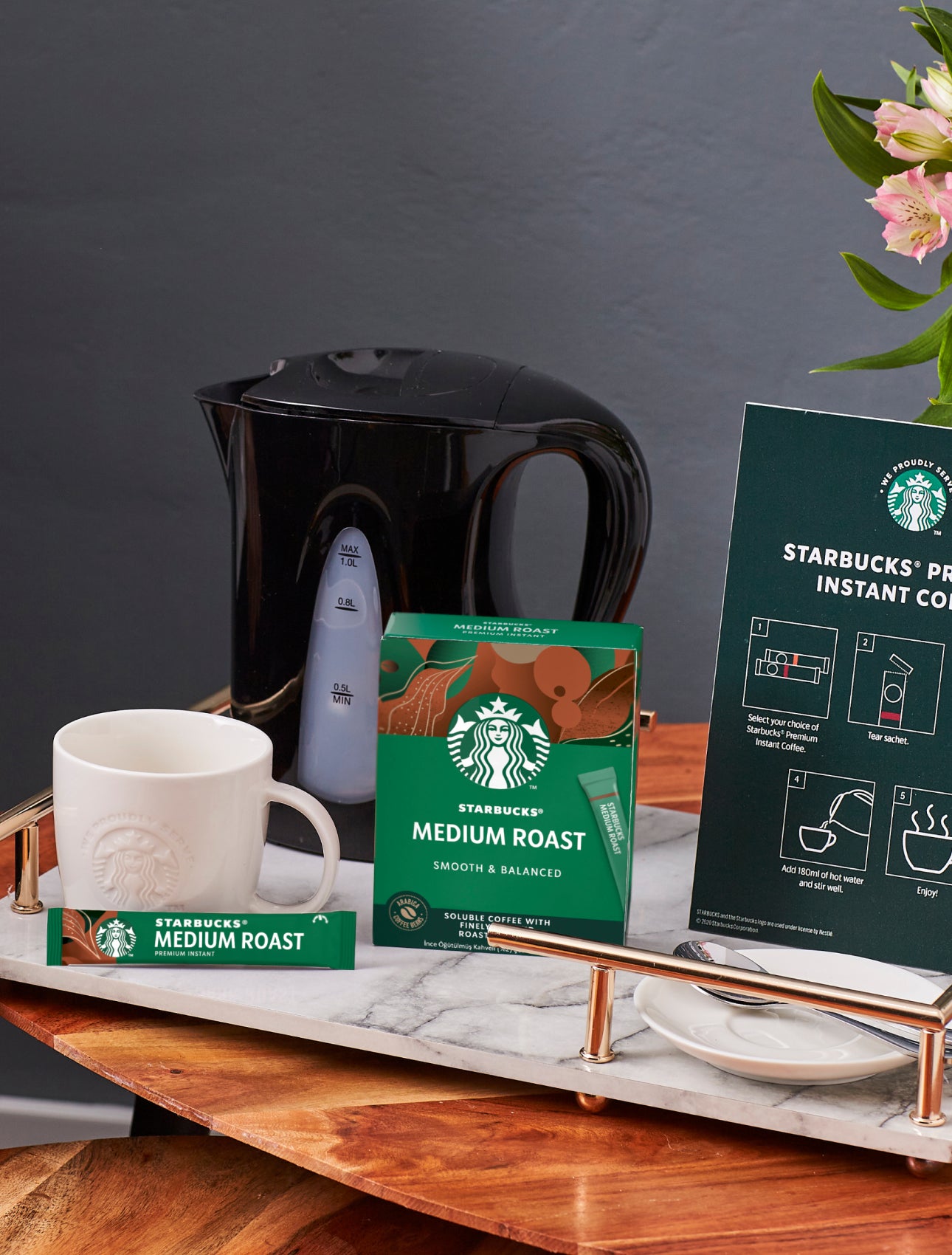 En bordplade med et We Proudly Serve Starbucks-krus, Starbucks Premium Instant Coffee og en tilberedningsvejledning