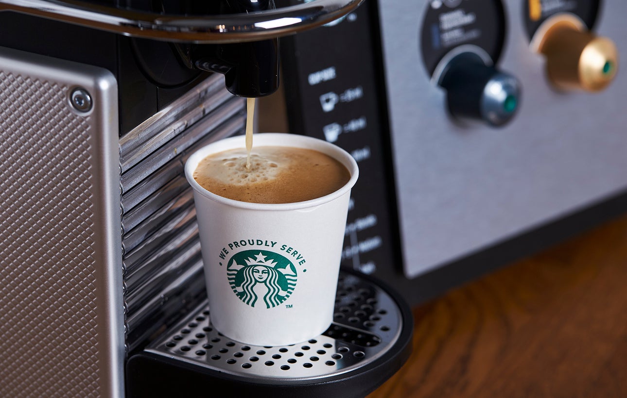 Et We Proudly Serve Starbucks-papbæger fyldes med friskbrygget kaffe fra en espressomaskine