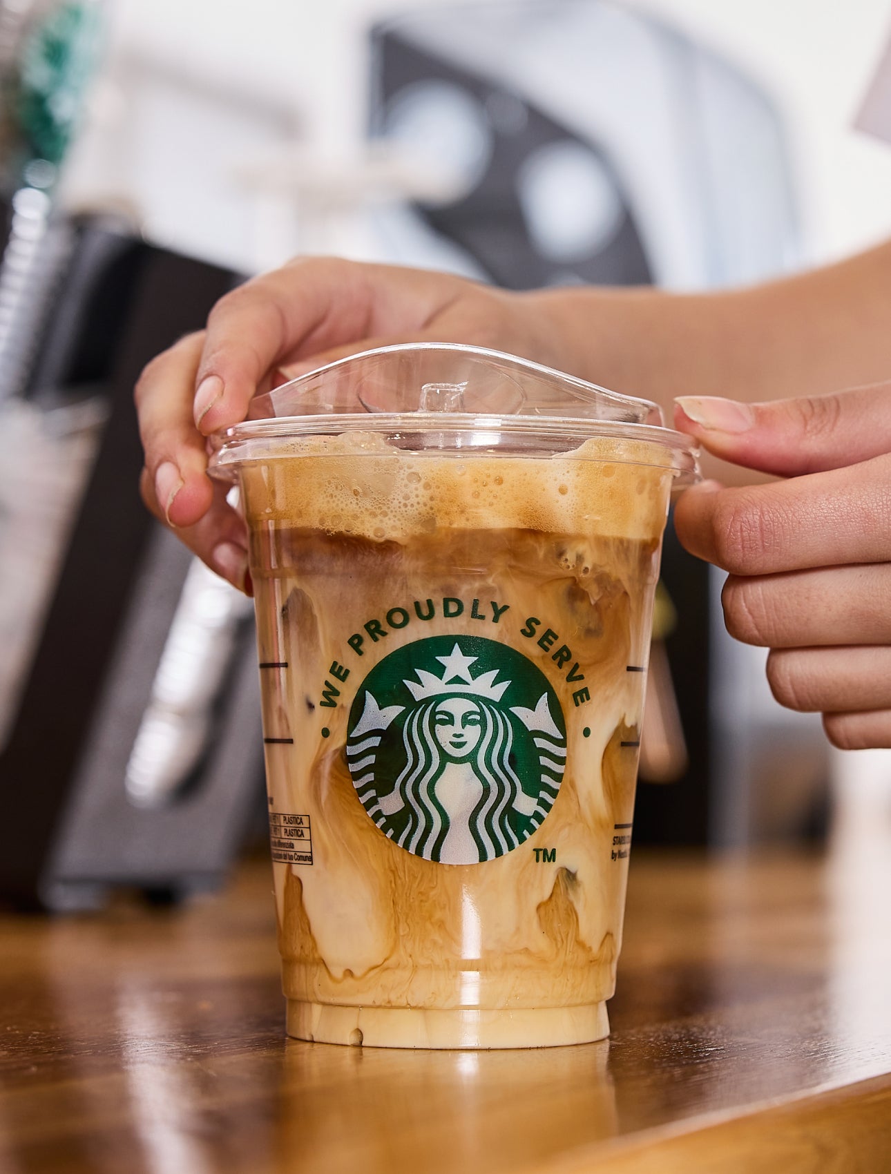 En barista sætter låg på en We Proudly Serve Starbucks-iskaffe med hvirvler af fløde og kaffe