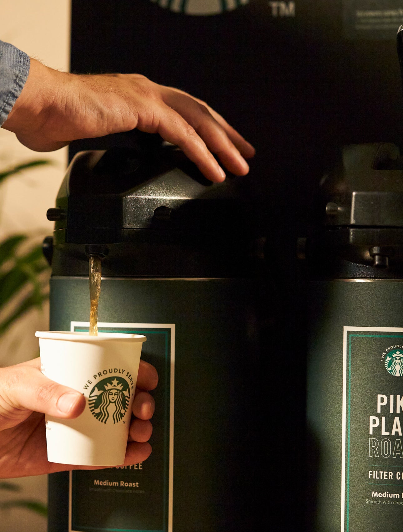 En person serverer Starbucks Pike Place® Roast-kaffe fra en stor kaffeautomat i et We Proudly Serve Starbucks-bæger