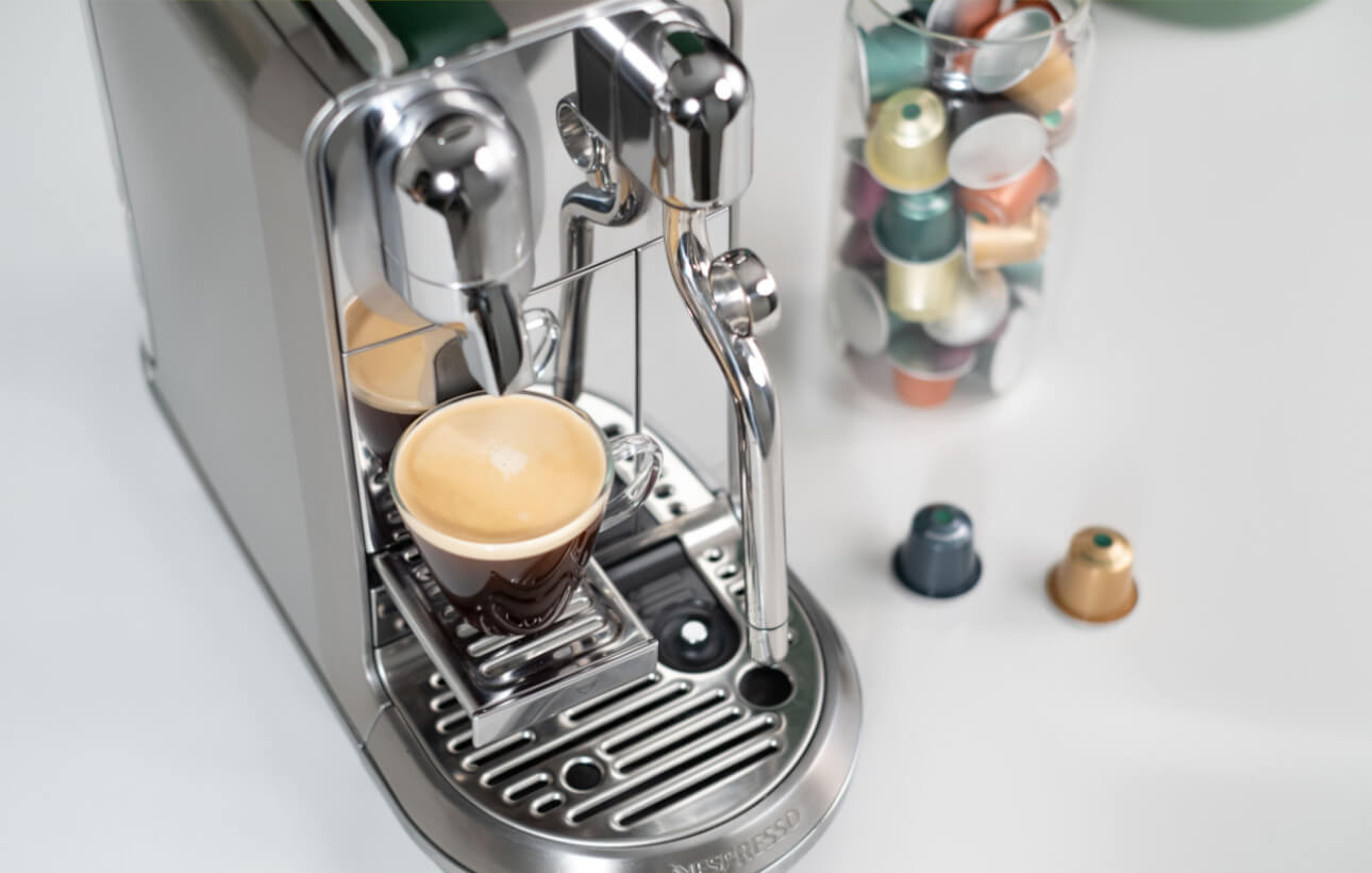 Nespresso-maskine med kaffe og We Proudly Serve Starbucks-kapsler i baggrunden