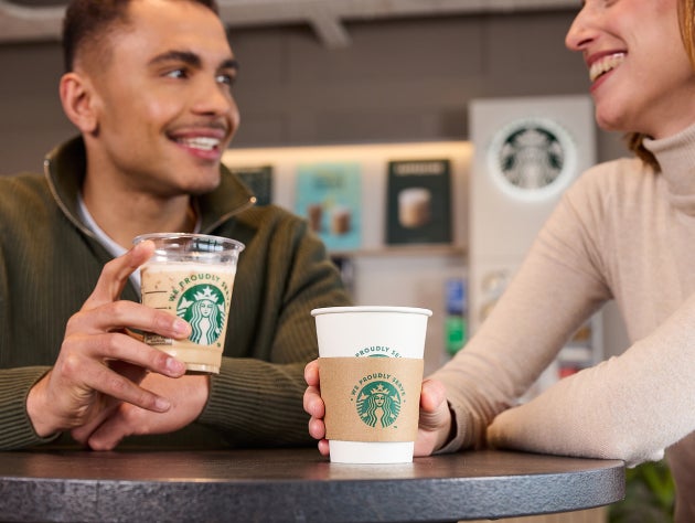 To personer som holder We Proudly Serve Starbucks-drikker på en kafé
