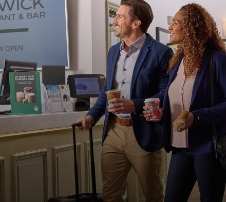 En mand og en kvinde går gennem en hotellobby med Starbucks-drikke