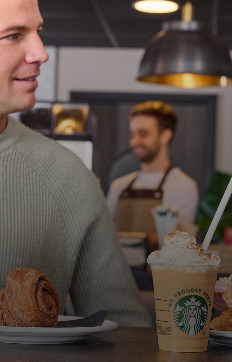 En mand og en kvinde smiler til hinanden på en café, mens de nyder Starbucks-kaffe