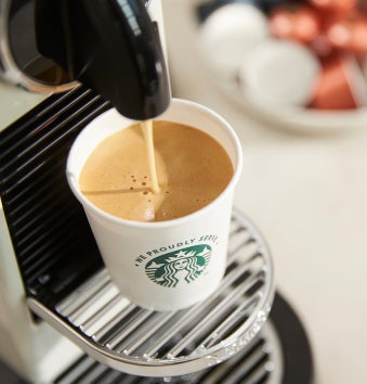 Et We Proudly Serve Starbucks-bæger fyldes med friskbrygget kaffe fra en espressomaskine til enkeltserveringer