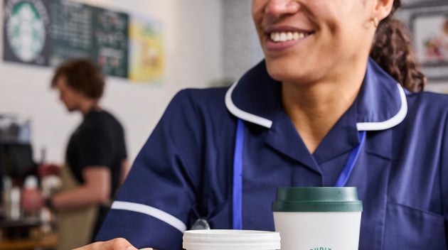 Sundhedspersonale sidder sammen i en hospitalscafé og holder drikke fra We Proudly Serve Starbucks i hænderne. 