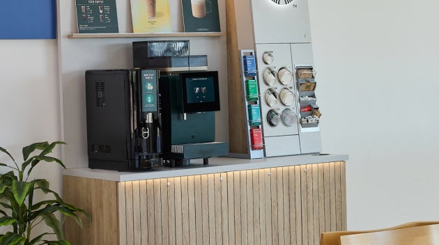 En kompakt We Proudly Serve Starbucks-kaffestation i et hospitalsambulatorium med en kaffestation med selvbetjening